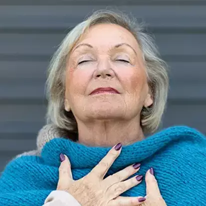 An elderly woman doing breathing exercises as she works on her respiratory health.