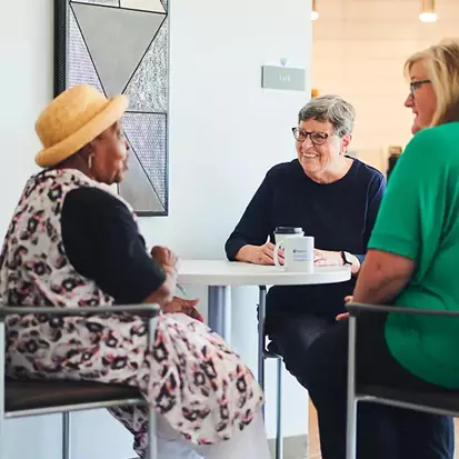 Three senior women having coffee and laughing at the SeniorSelect Center.